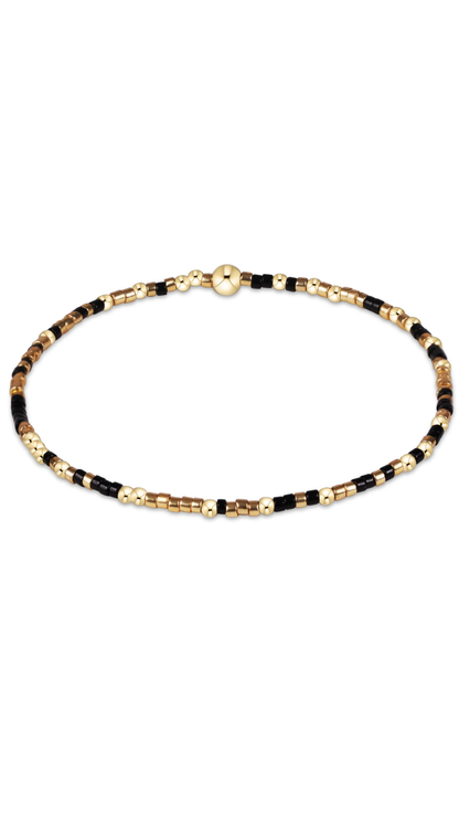 A beaded necklace featuring alternating segments of black beads, metallic gold beads, and textured brown beads, arranged in a circular shape on a plain white background.