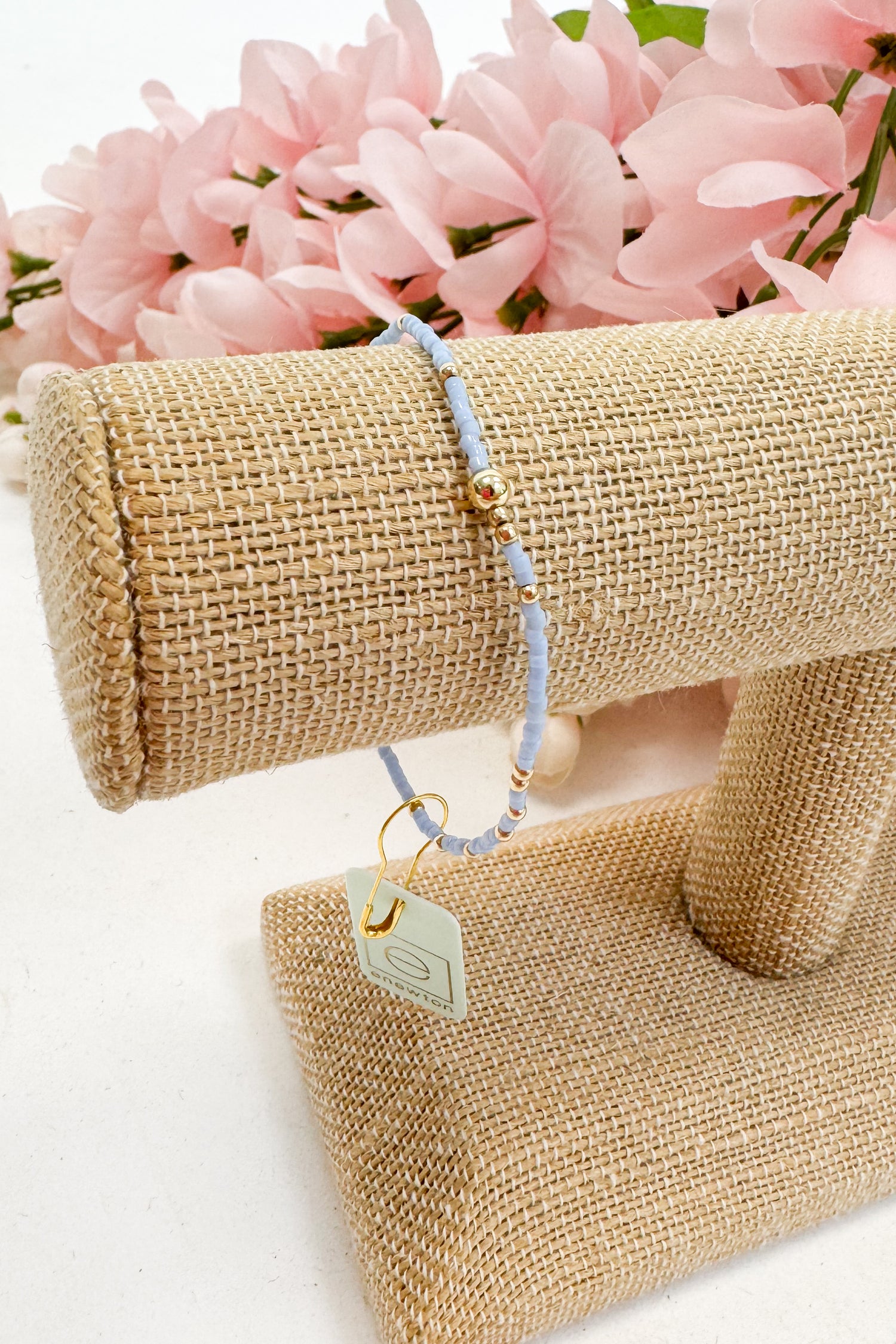 light blue Beaded bracelet on a beige jewelry display with pink flowers in the background