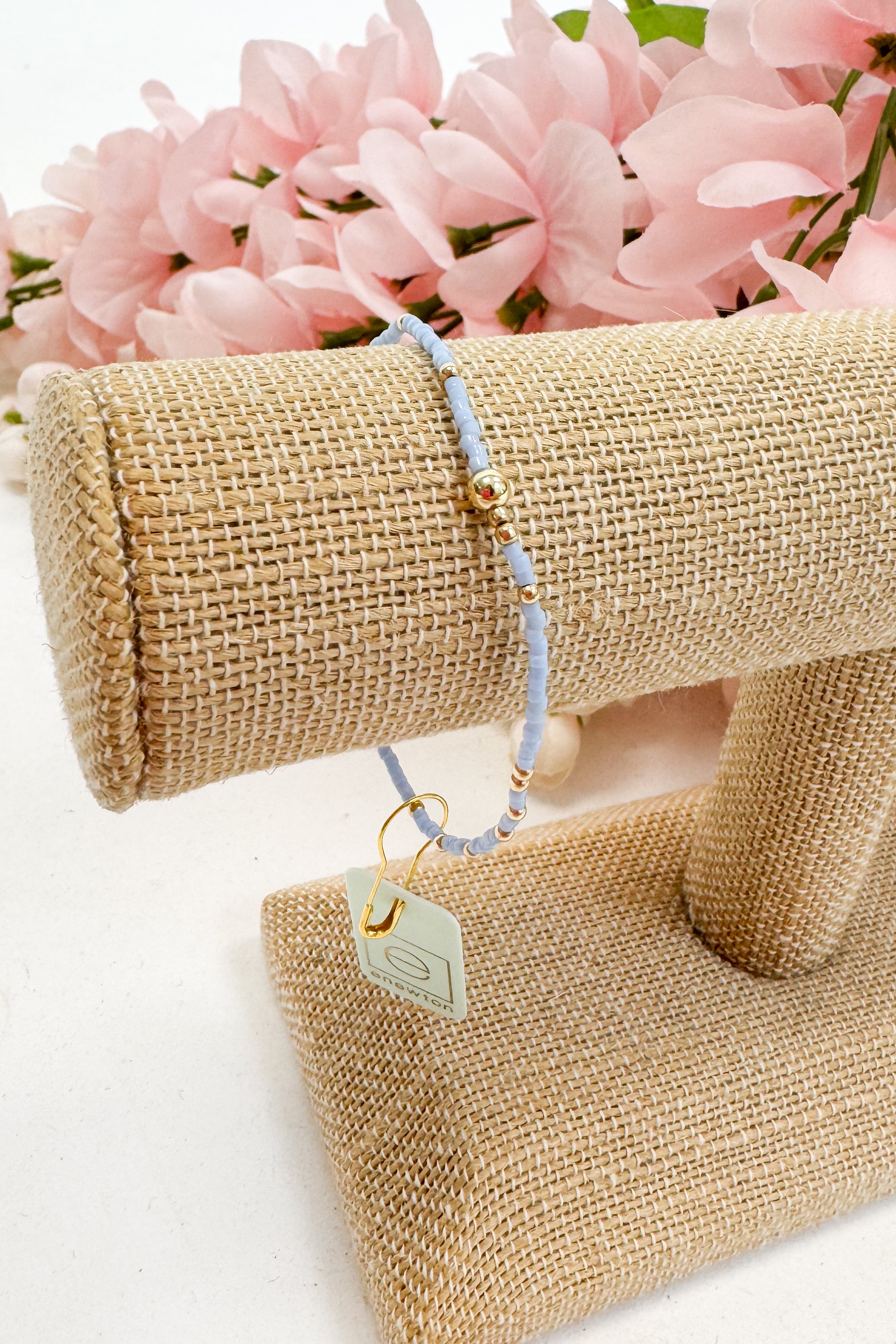 light blue Beaded bracelet on a beige jewelry display with pink flowers in the background