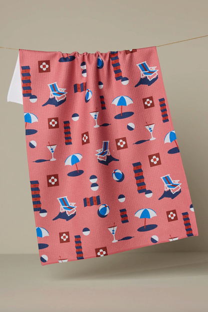 Light red towel with beach-themed pattern hanging on a line against a beige background
