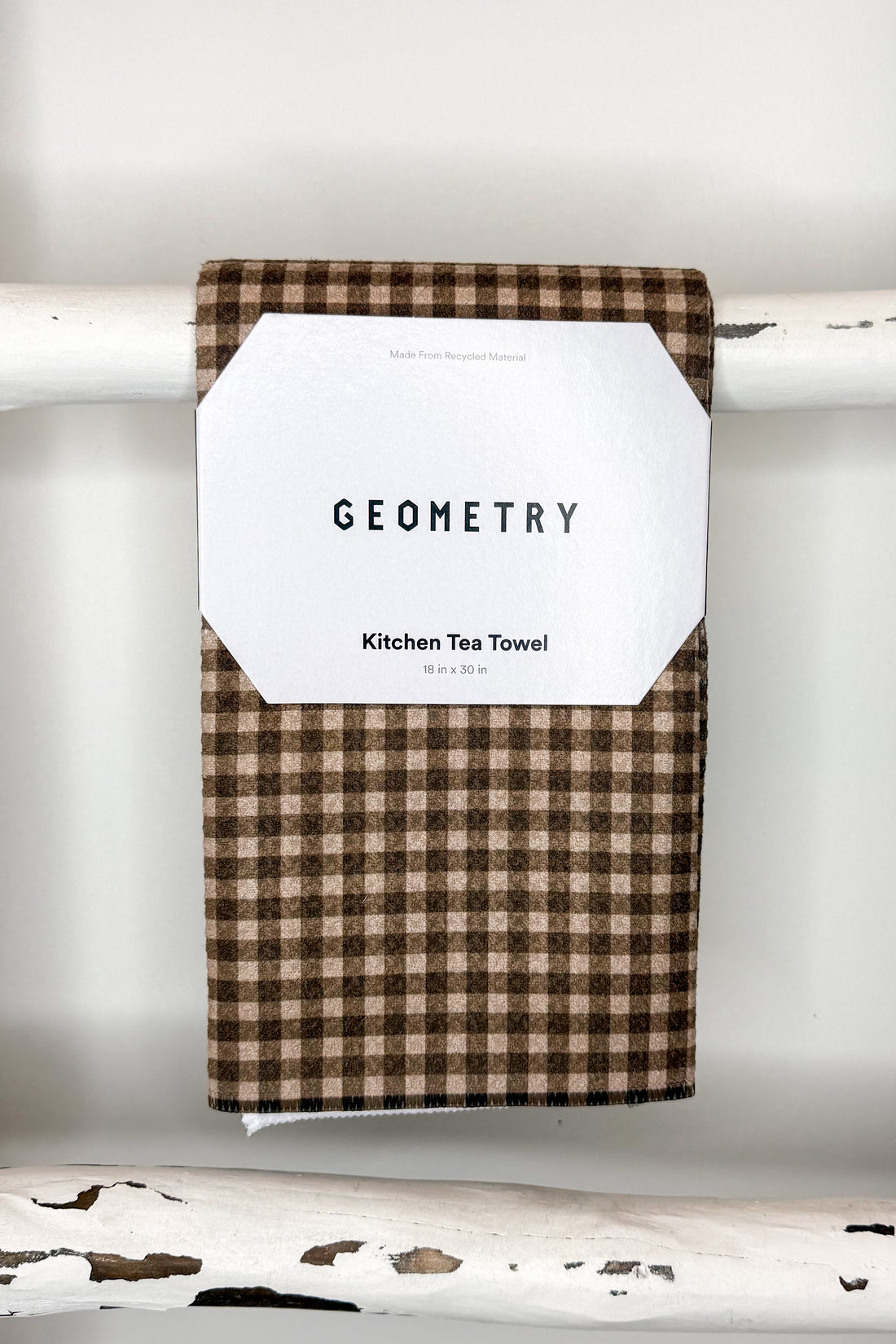 A brown and beige gingham kitchen tea towel with a white paper label that reads &