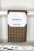 A brown and beige gingham kitchen tea towel with a white paper label that reads &