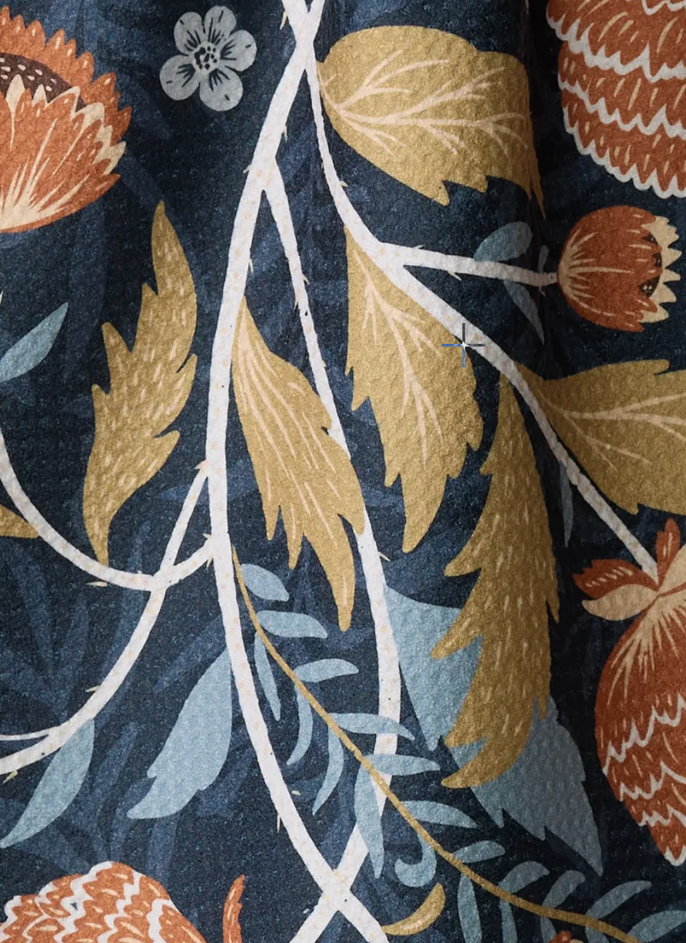 A close-up of a towel pattern featuring stylized botanical elements, including gold leaves, rust-orange flowers, and pale blue foliage on a dark navy background.