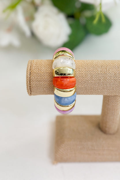 Multicolored beaded bracelet on a burlap stand with flowers in the background