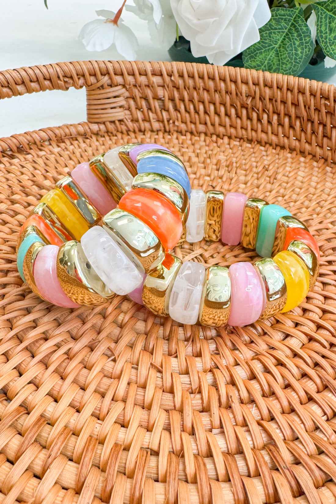 Colorful beaded bracelet on a woven surface with flowers in the background