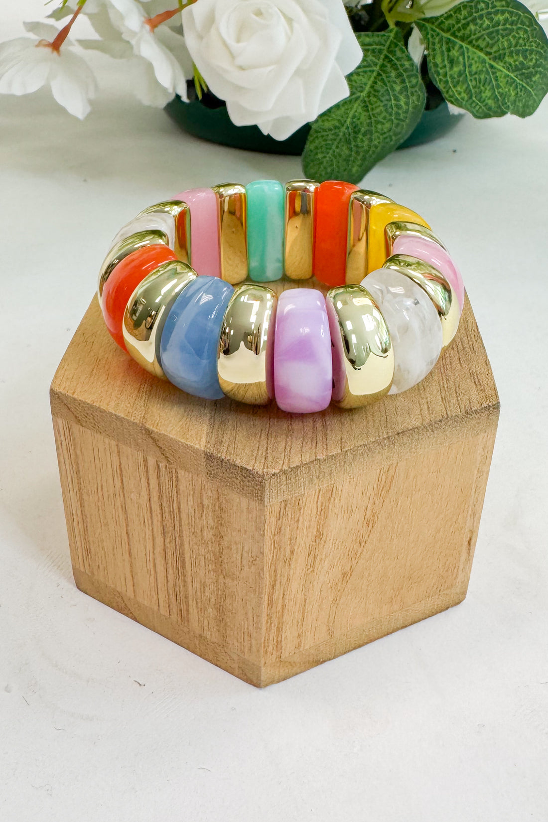Colorful beaded bracelet on a wooden block with flowers in the background