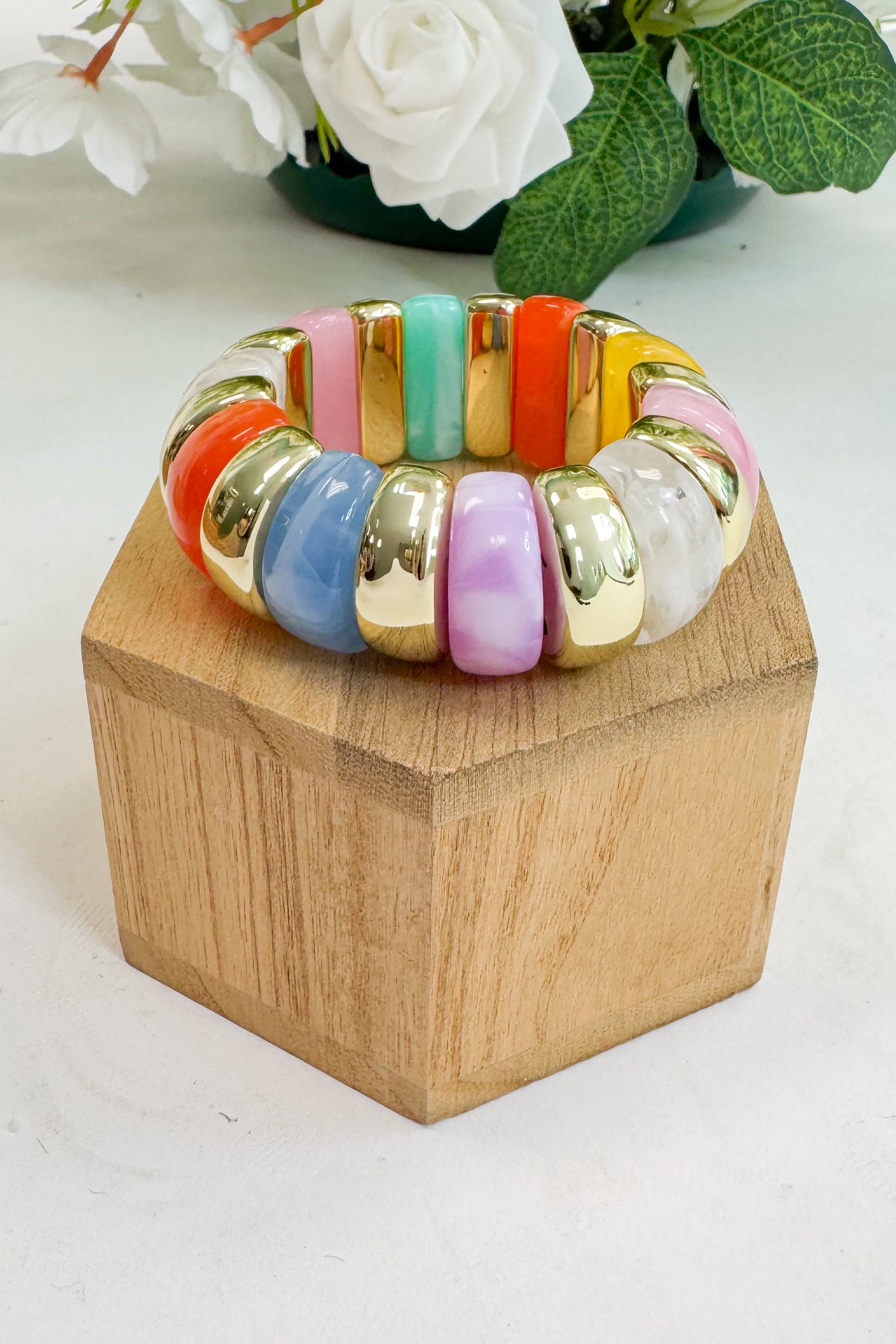 Colorful beaded bracelet on a wooden block with flowers in the background