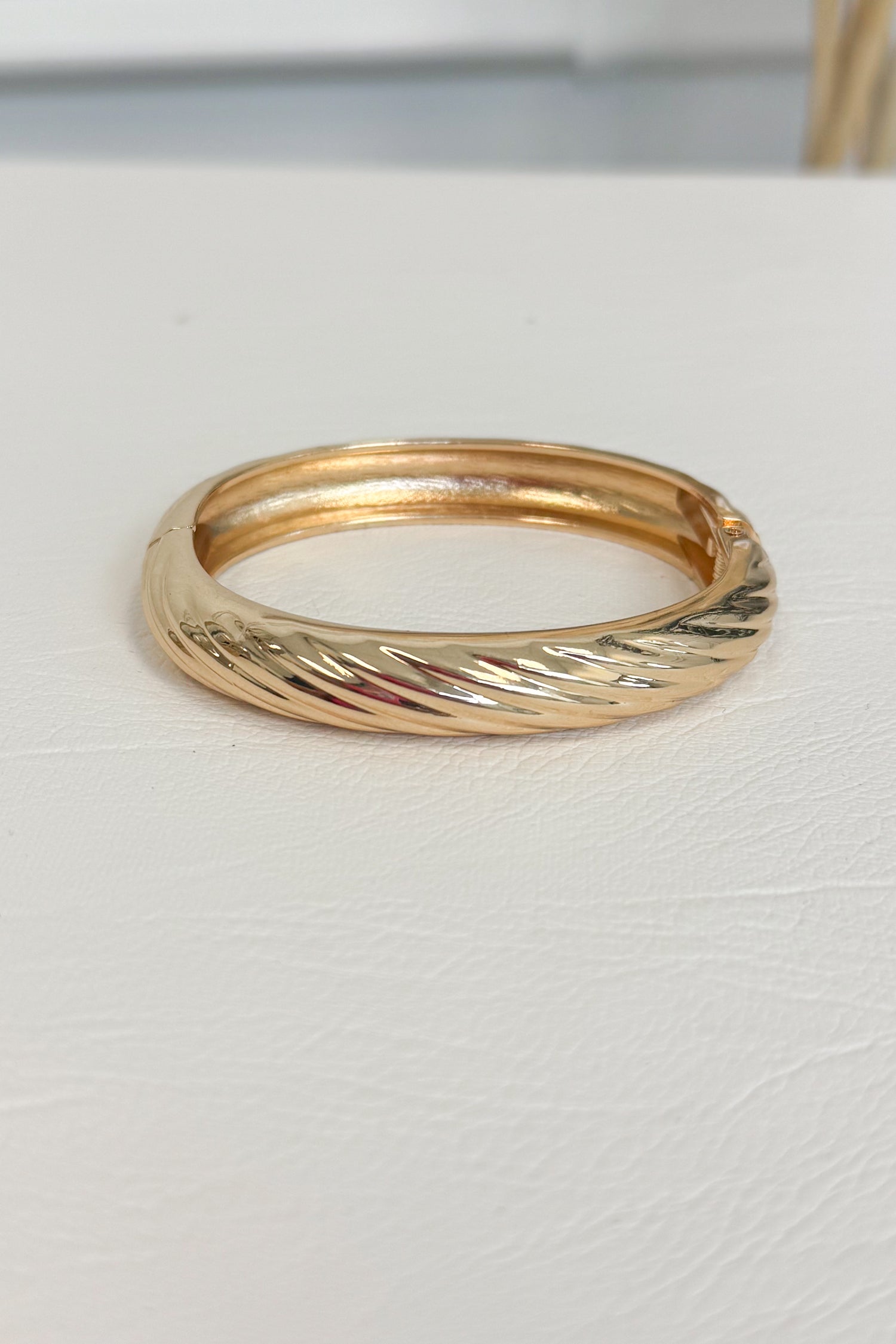 Gold-tone polished bracelet with a simple smooth, rounded band design on a white studio background