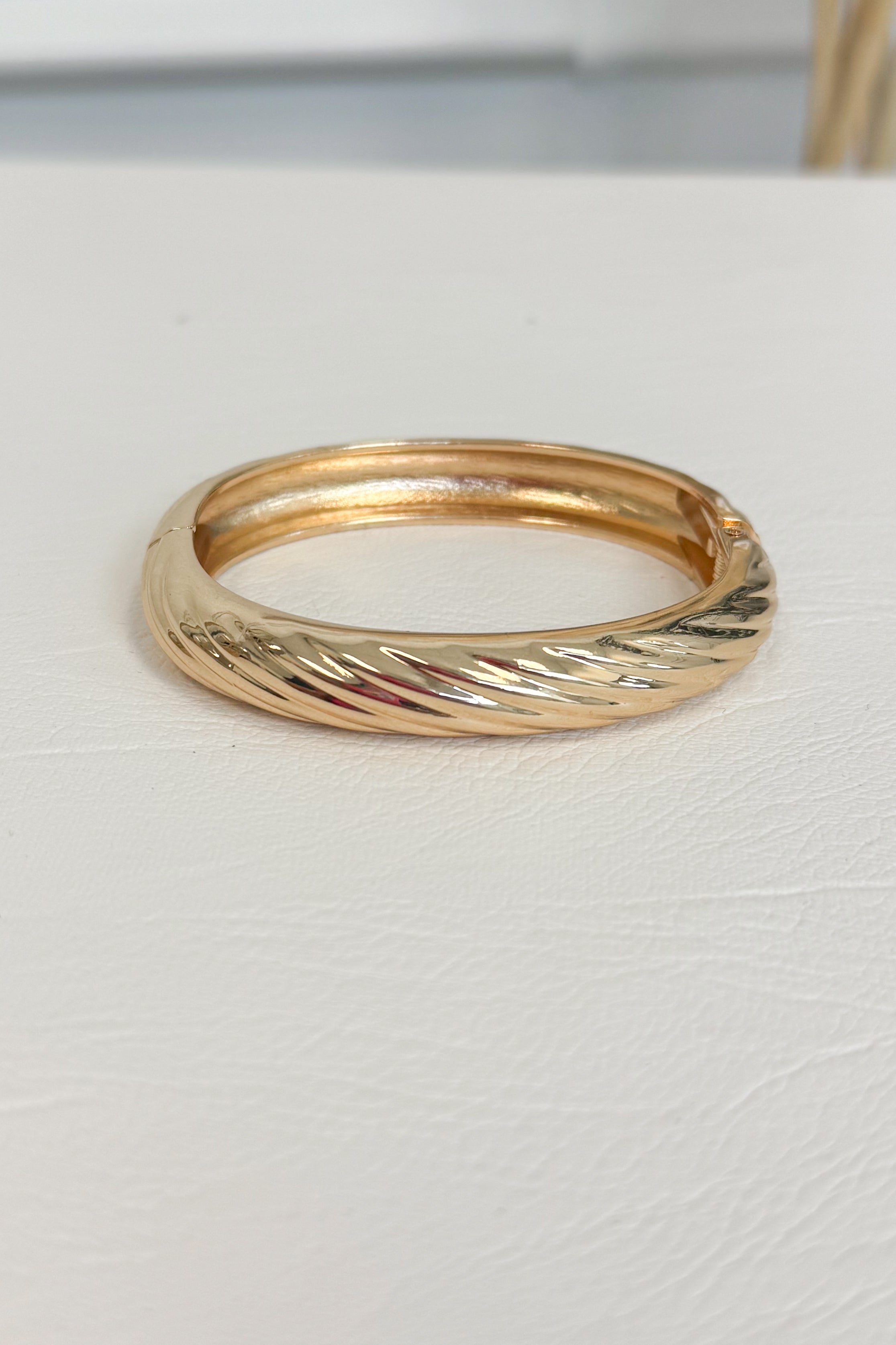 Gold-tone polished bracelet with a simple smooth, rounded band design on a white studio background