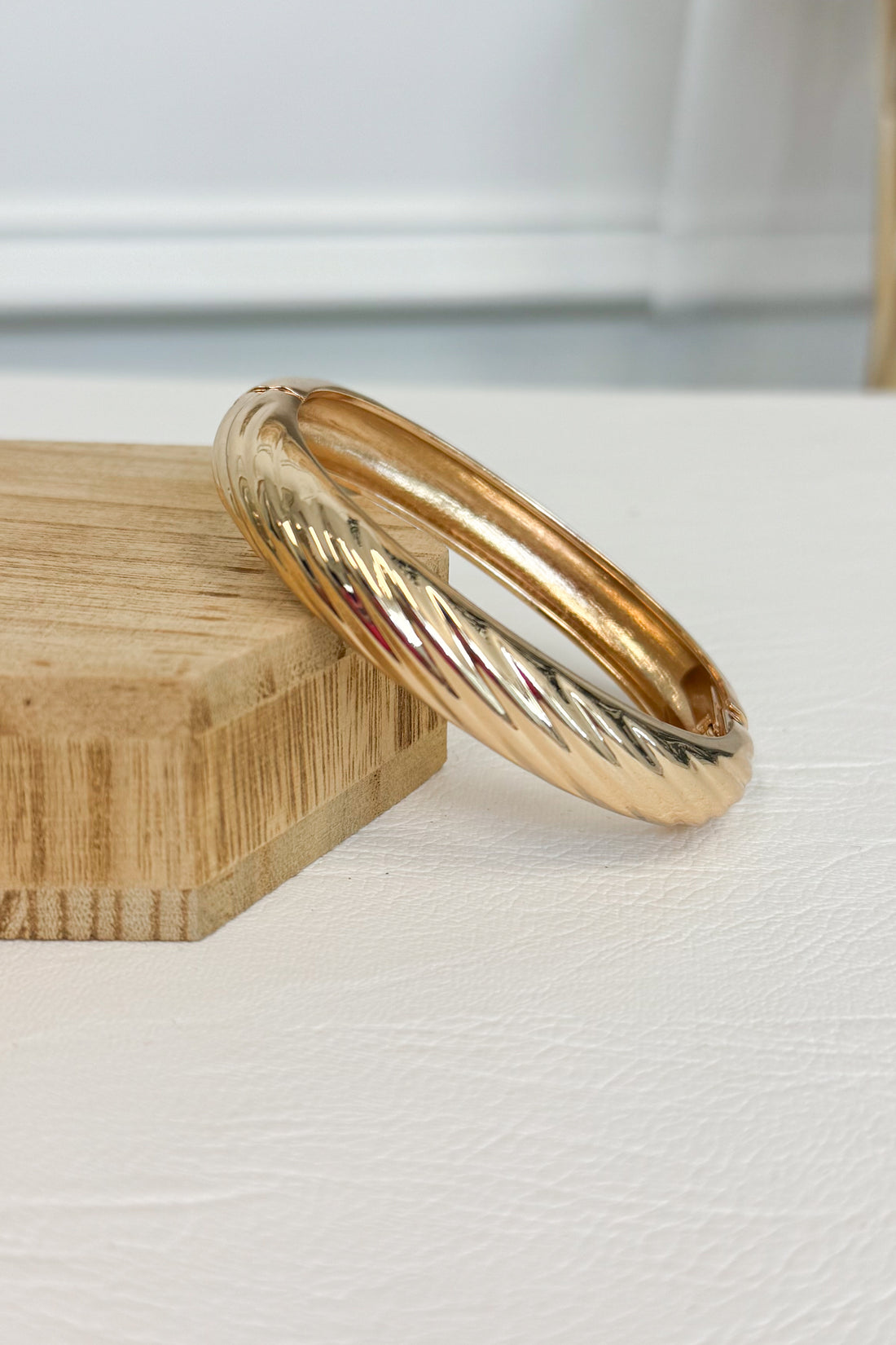 Gold-tone bracelet with a raised textured design and smooth rounded edges on a white studio background