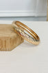 Gold-tone bracelet with a raised textured design and smooth rounded edges on a white studio background