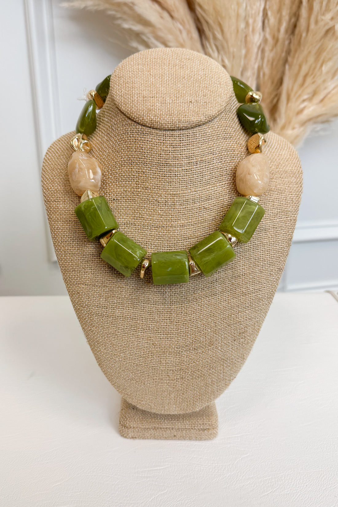 front view of green statement necklace with small gold and cream accents displayed of bust 