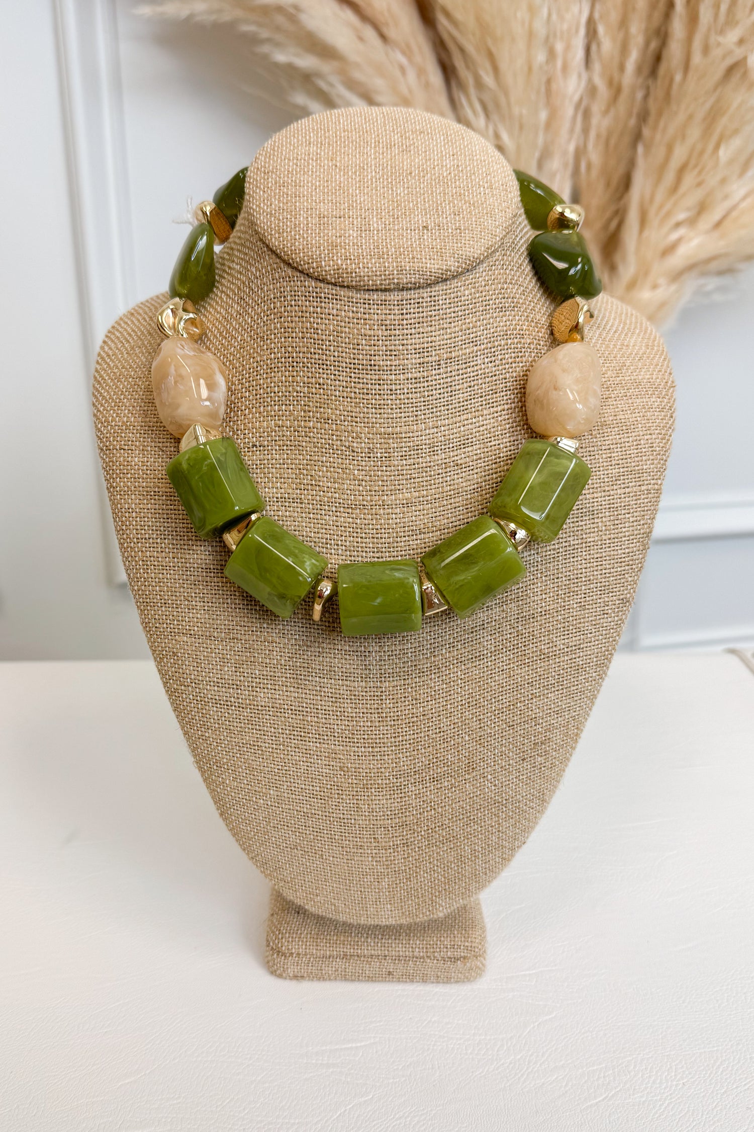 front view of green statement necklace with small gold and cream accents displayed of bust 