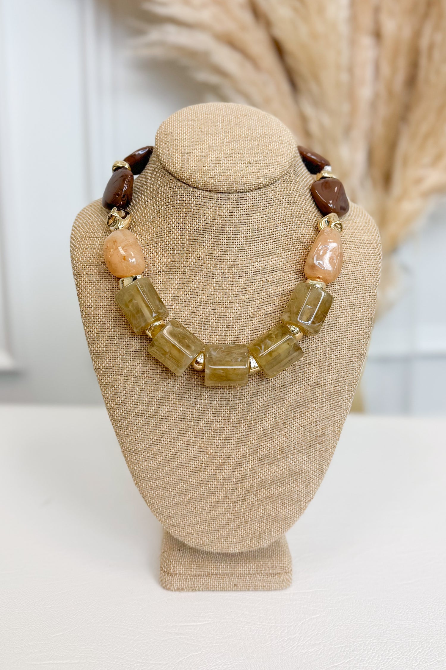 front view of chunky olive, soft peach, and brown beaded necklace with gold accents on bust
