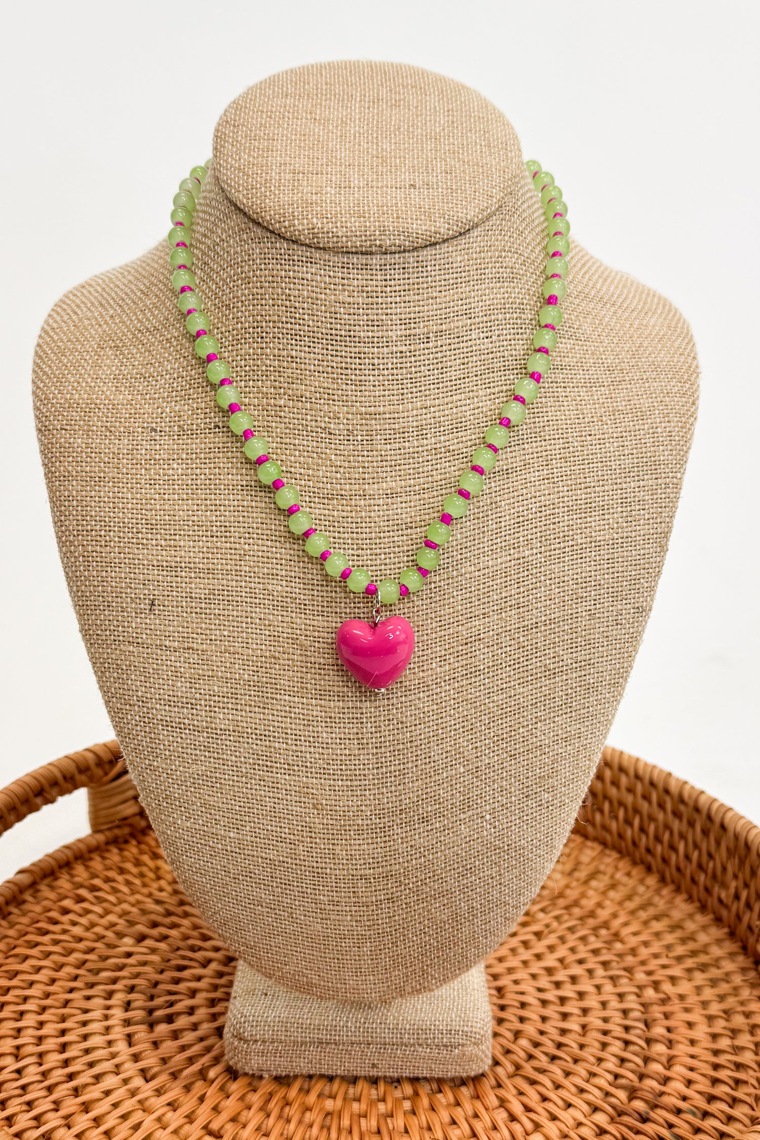 Necklace with a pink heart pendant on a beige bust against a white background