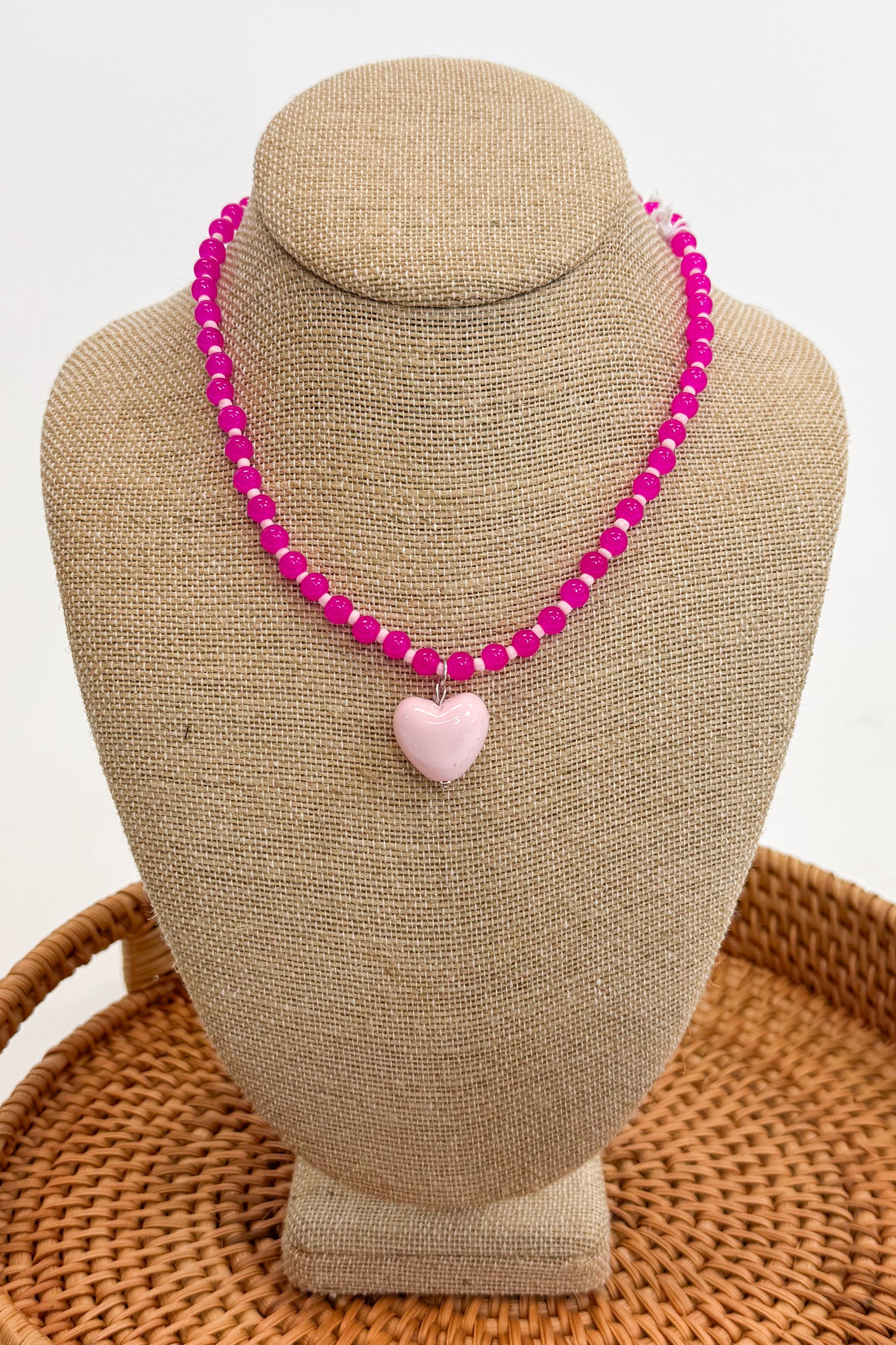 Necklace with pink beads and a heart-shaped charm on a beige bust against a white background