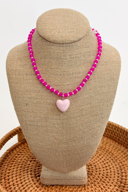 Necklace with pink beads and a heart-shaped charm on a beige bust against a white background
