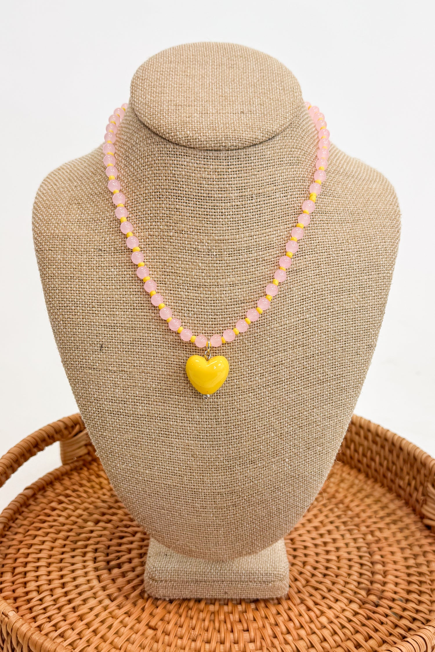 Necklace with a yellow heart pendant on a beige bust against a white background