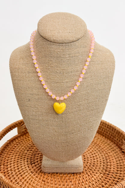 Necklace with a yellow heart pendant on a beige bust against a white background