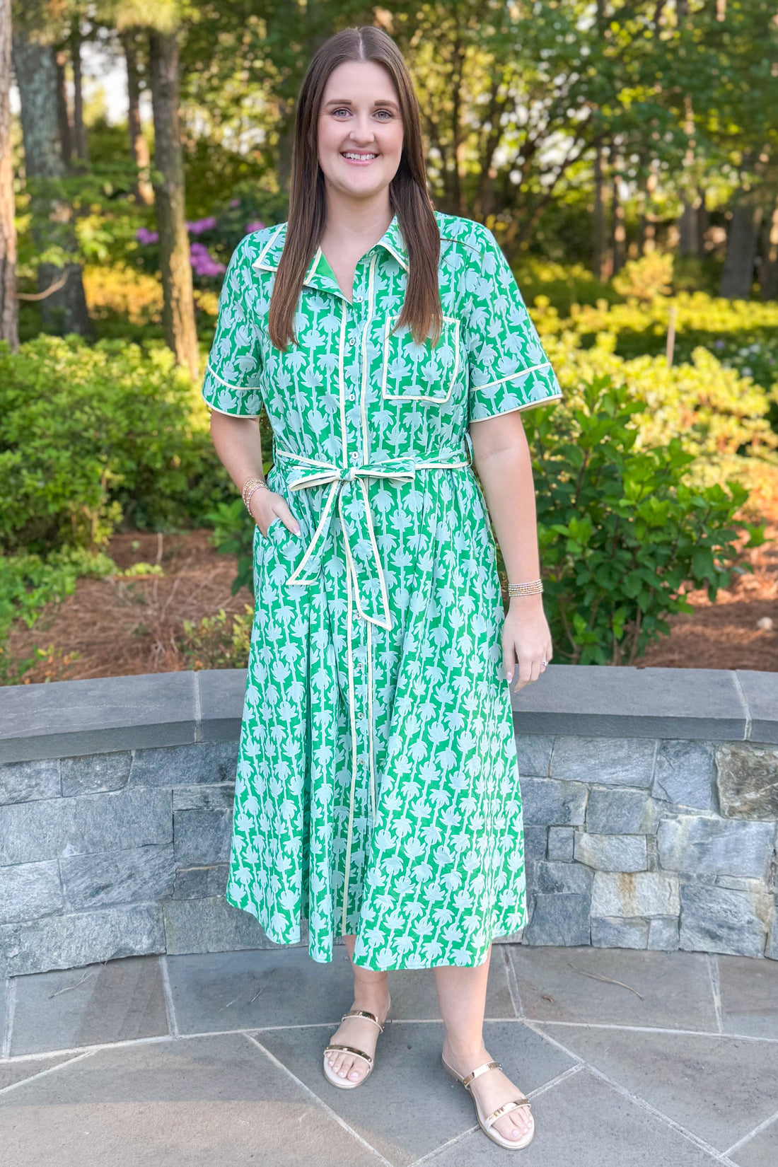 woman wearing green printed button down midi dress with tie detailing standing outside.