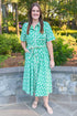 woman wearing green printed button down midi dress with tie detailing standing outside.