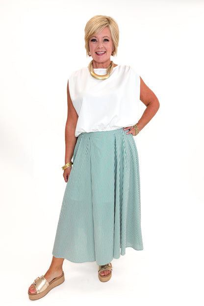 Front view of woman wearing Swagger Boutique’s Green Striped Flowy Midi Skirt with white top against white studio background.