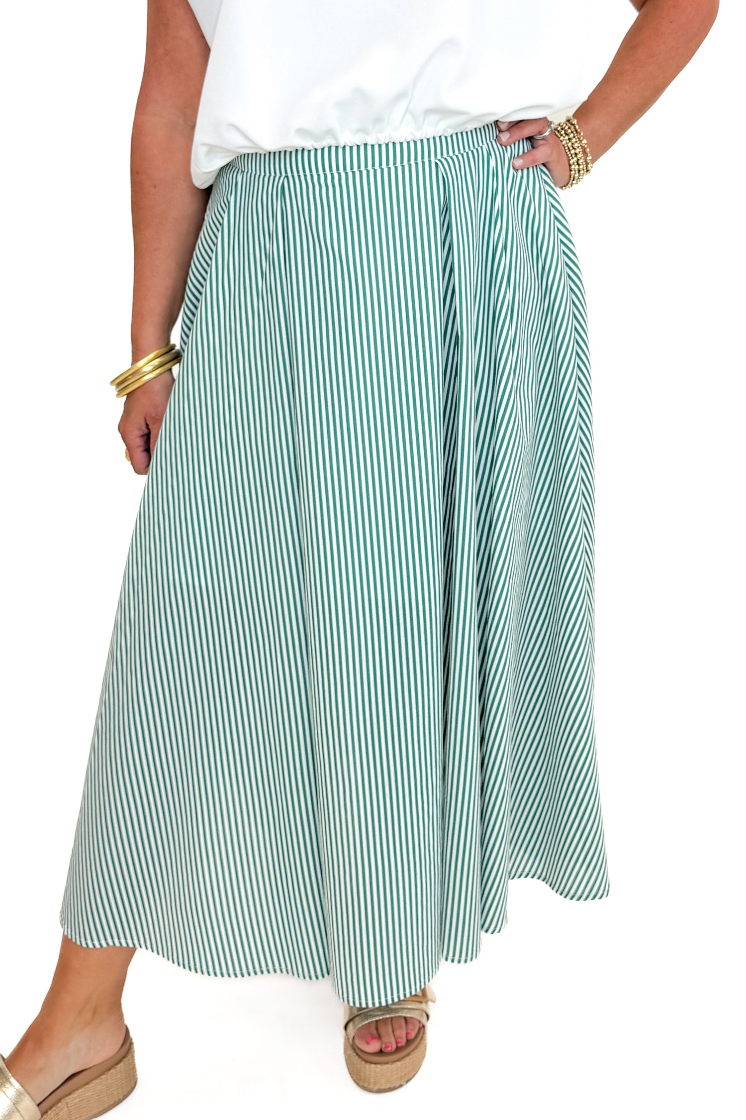 Front detail view of woman wearing Swagger Boutique’s Green Striped Flowy Midi Skirt with white top against white studio background.
