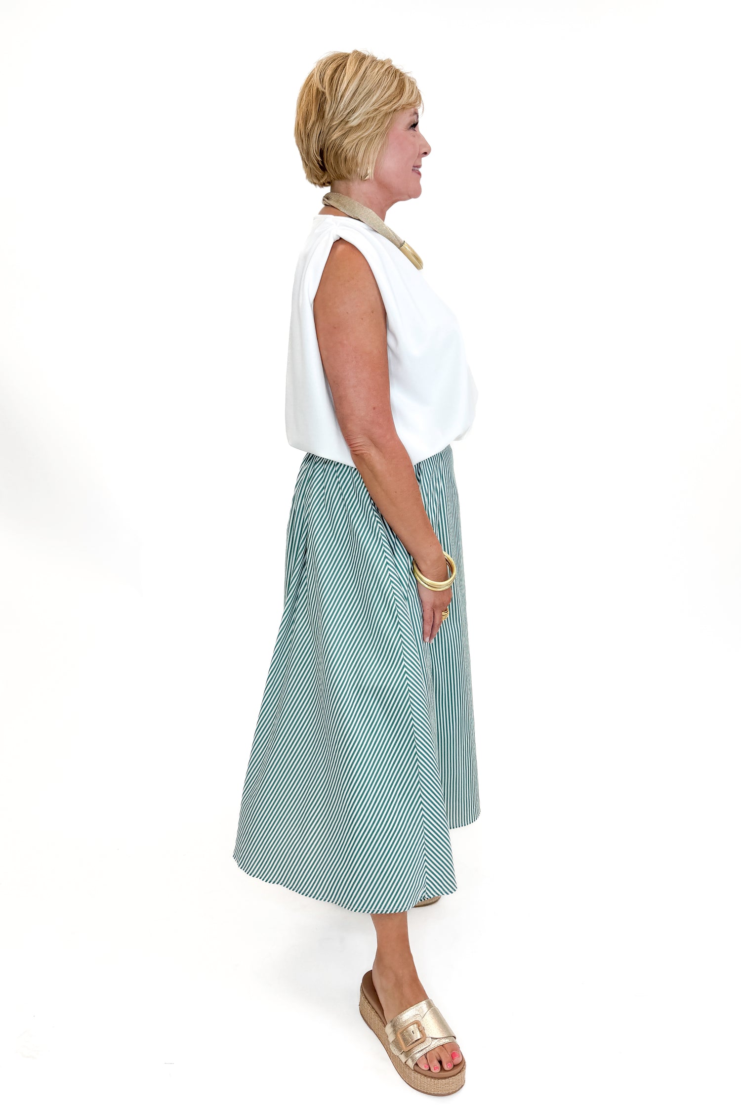 Side view of woman wearing Swagger Boutique’s Green Striped Flowy Midi Skirt with white top against white studio background.