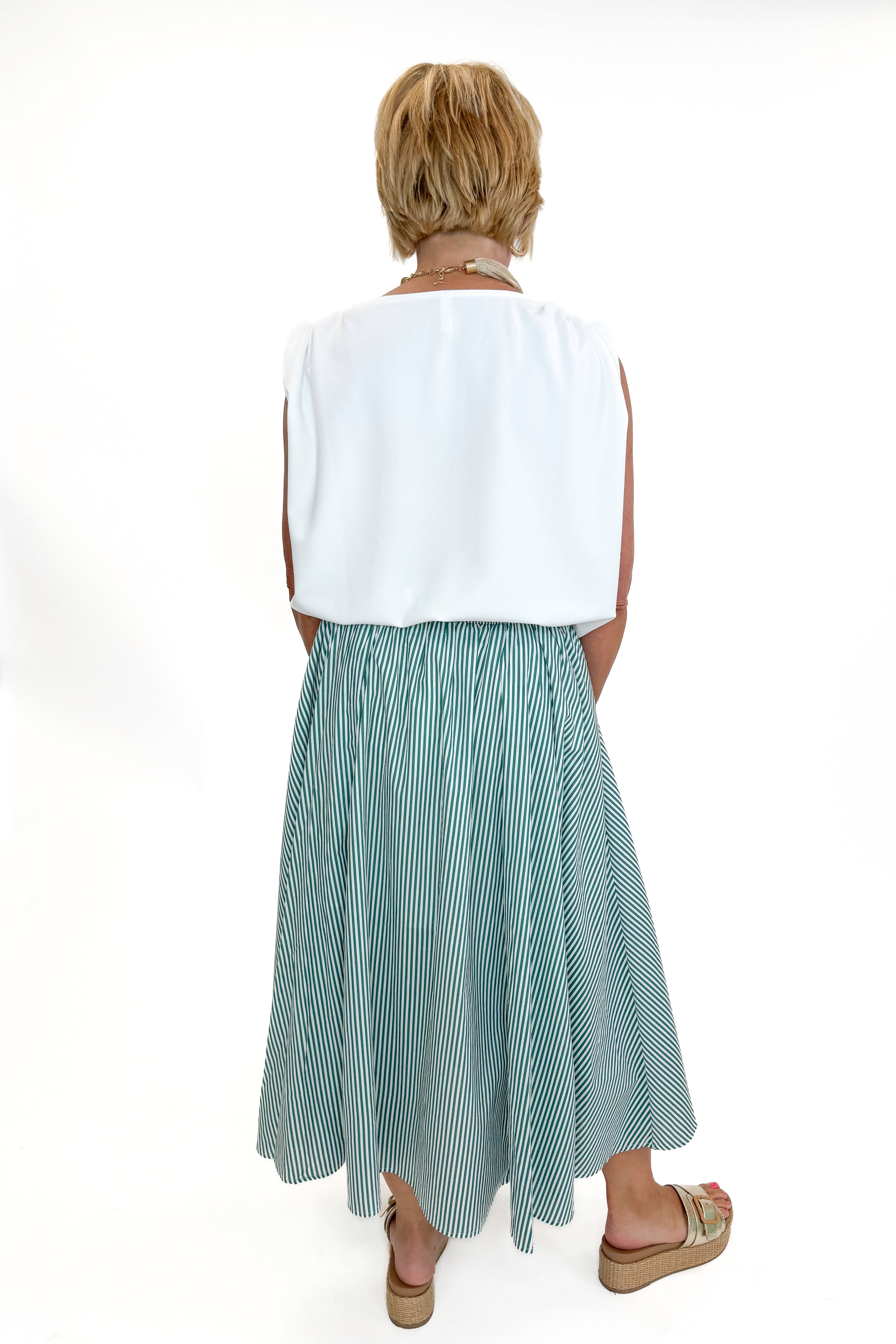 Back view of woman wearing Swagger Boutique’s Green Striped Flowy Midi Skirt with white top against white studio background.