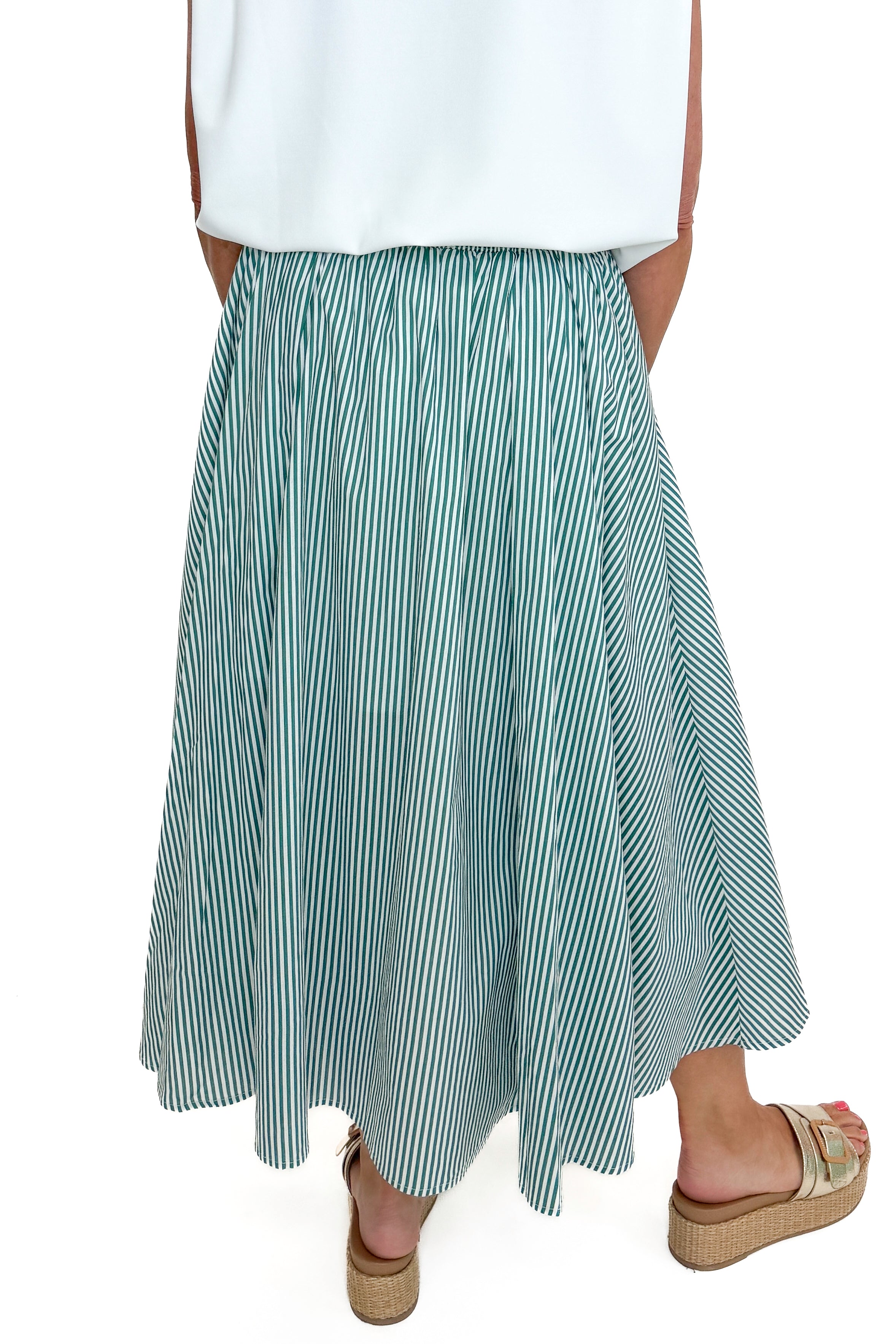 Back detail view of woman wearing Swagger Boutique’s Green Striped Flowy Midi Skirt with white top against white studio background.