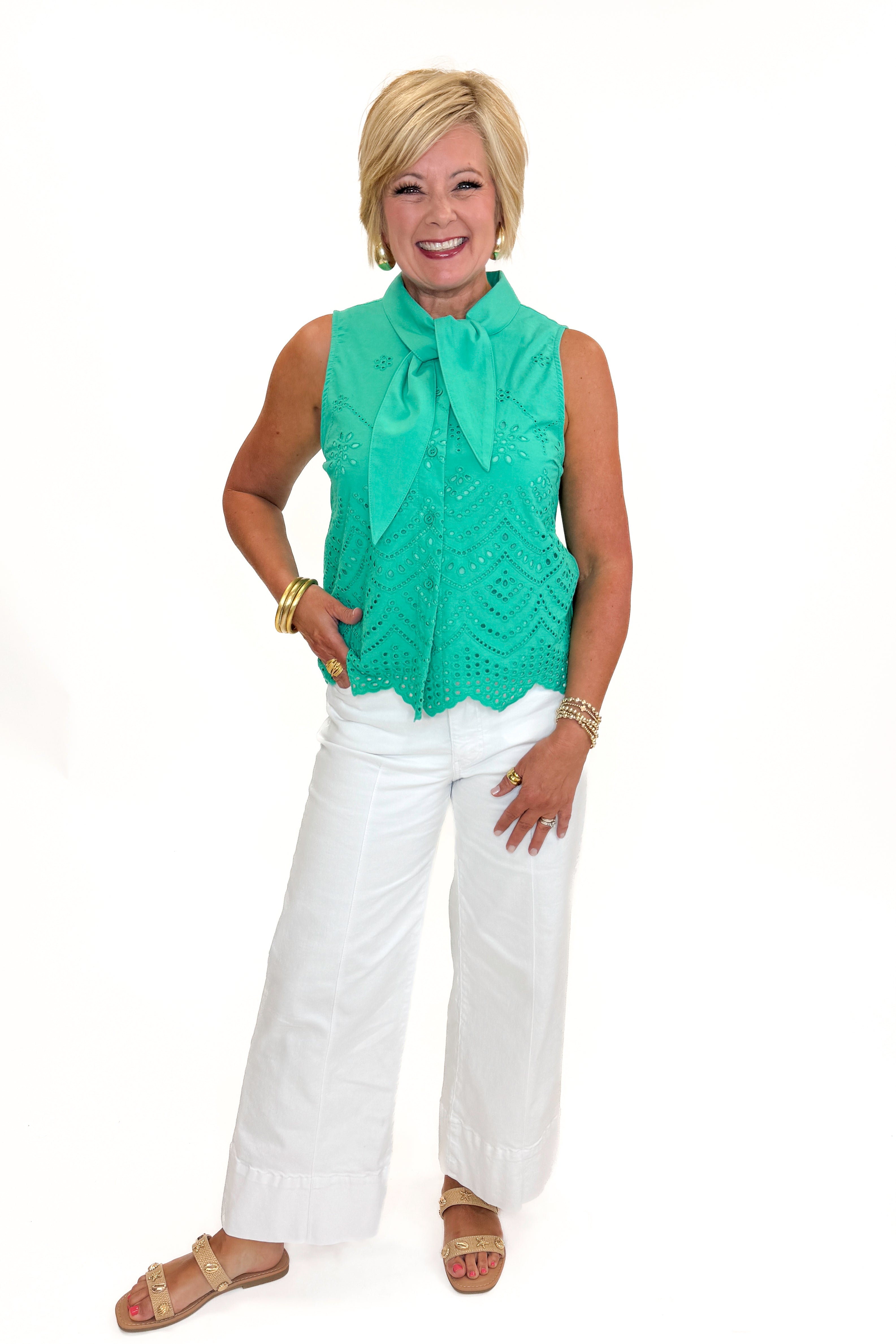 Front view of woman wearing Swagger Boutique’s Green Tie Neck Eyelet Sleeveless Top with jeans against white studio background.
