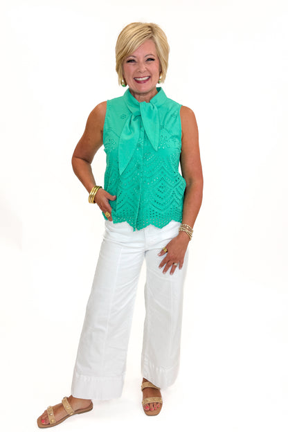 Front view of woman wearing Swagger Boutique’s Green Tie Neck Eyelet Sleeveless Top with jeans against white studio background.