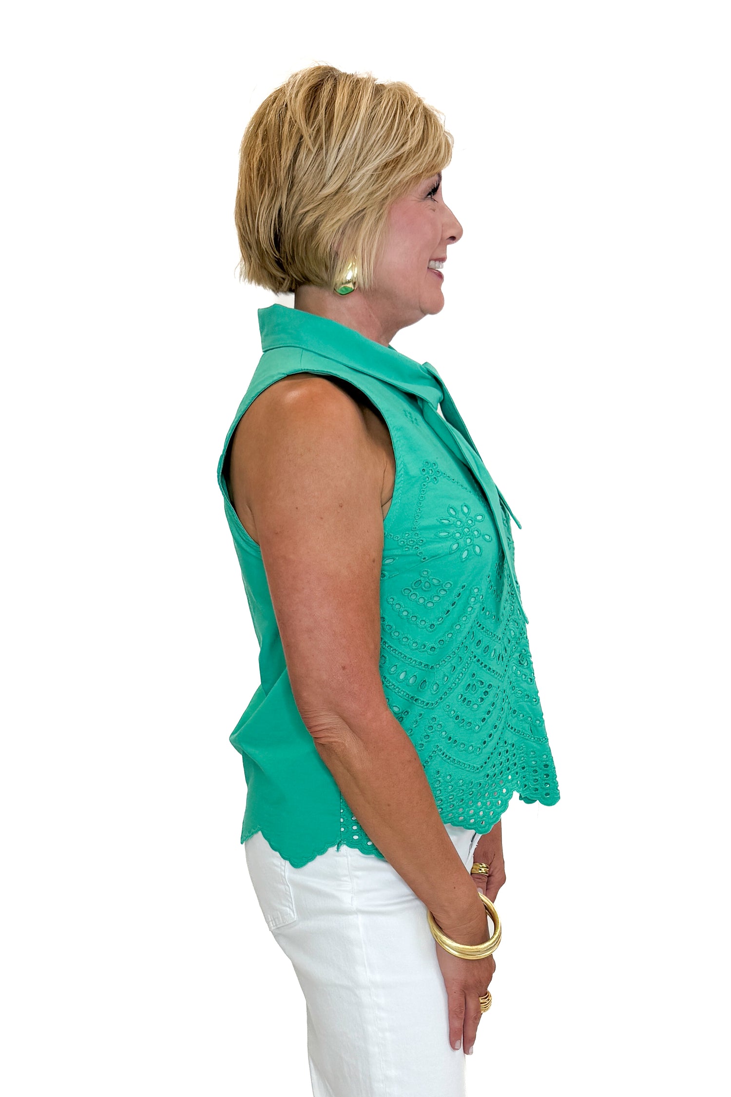 Side view of woman wearing Swagger Boutique’s Green Tie Neck Eyelet Sleeveless Top with jeans against white studio background.