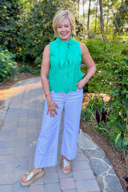 Front view of woman wearing Swagger Boutique’s Green Tie Neck Eyelet Sleeveless Top with jeans standing outside at a park.