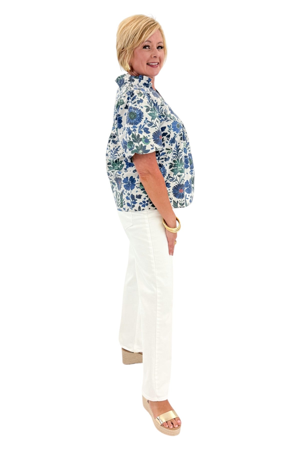 Side view of woman wearing Swagger Boutique’s Green &amp; Blue Floral V-Neck Top with sandals against white studio background.