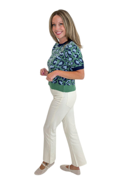 Side view of woman wearing Swagger Boutique’s Green &amp; Blue Leopard Short Sleeve Sweater with jeans against white studio background.