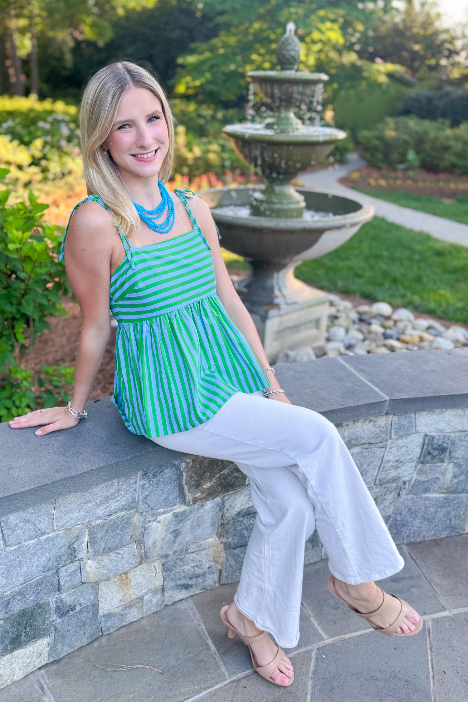 Front view of woman wearing Swagger Boutique’s Green &amp; Blue Striped Peplum Tank by Entro with jeans sitting outside at a park.