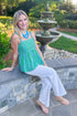 Front view of woman wearing Swagger Boutique’s Green & Blue Striped Peplum Tank by Entro with jeans sitting outside at a park.