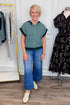 Front view of woman wearing Swagger Boutique’s Green & Blue Striped Sleeveless Sweater with jeans with clothing hanging in the background.