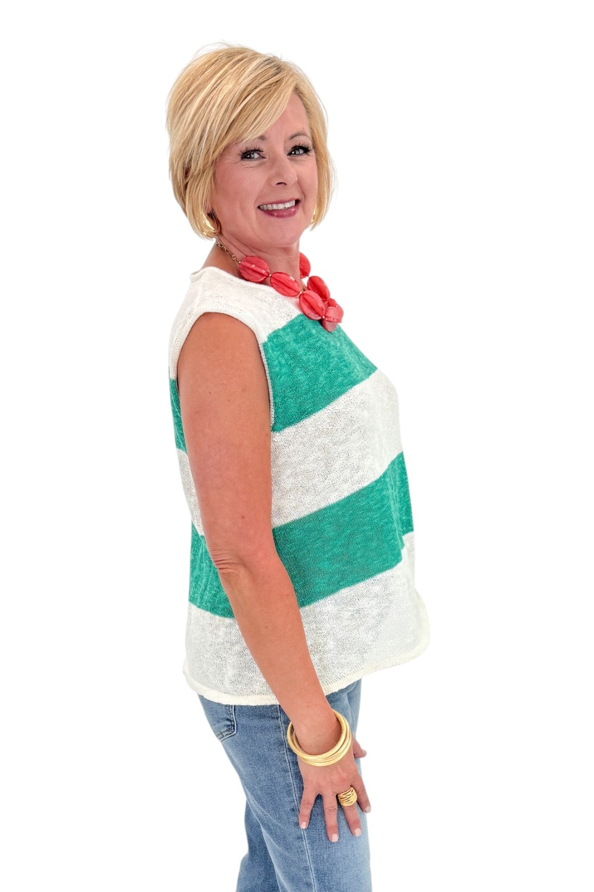 Side view of woman wearing Swagger Boutique’s Green &amp; White Striped Sleeveless Sweater with jeans against white studio background.
