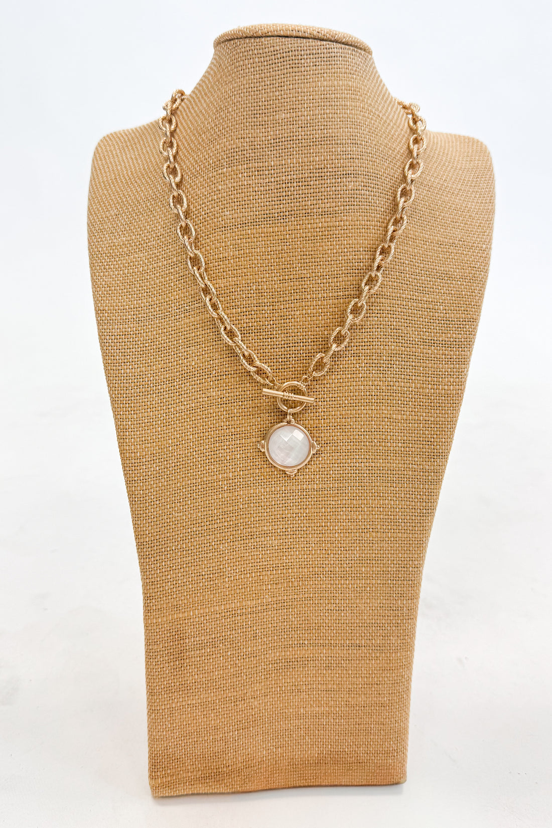 Gold chain necklace with a pendant on a brown mannequin bust against a white background