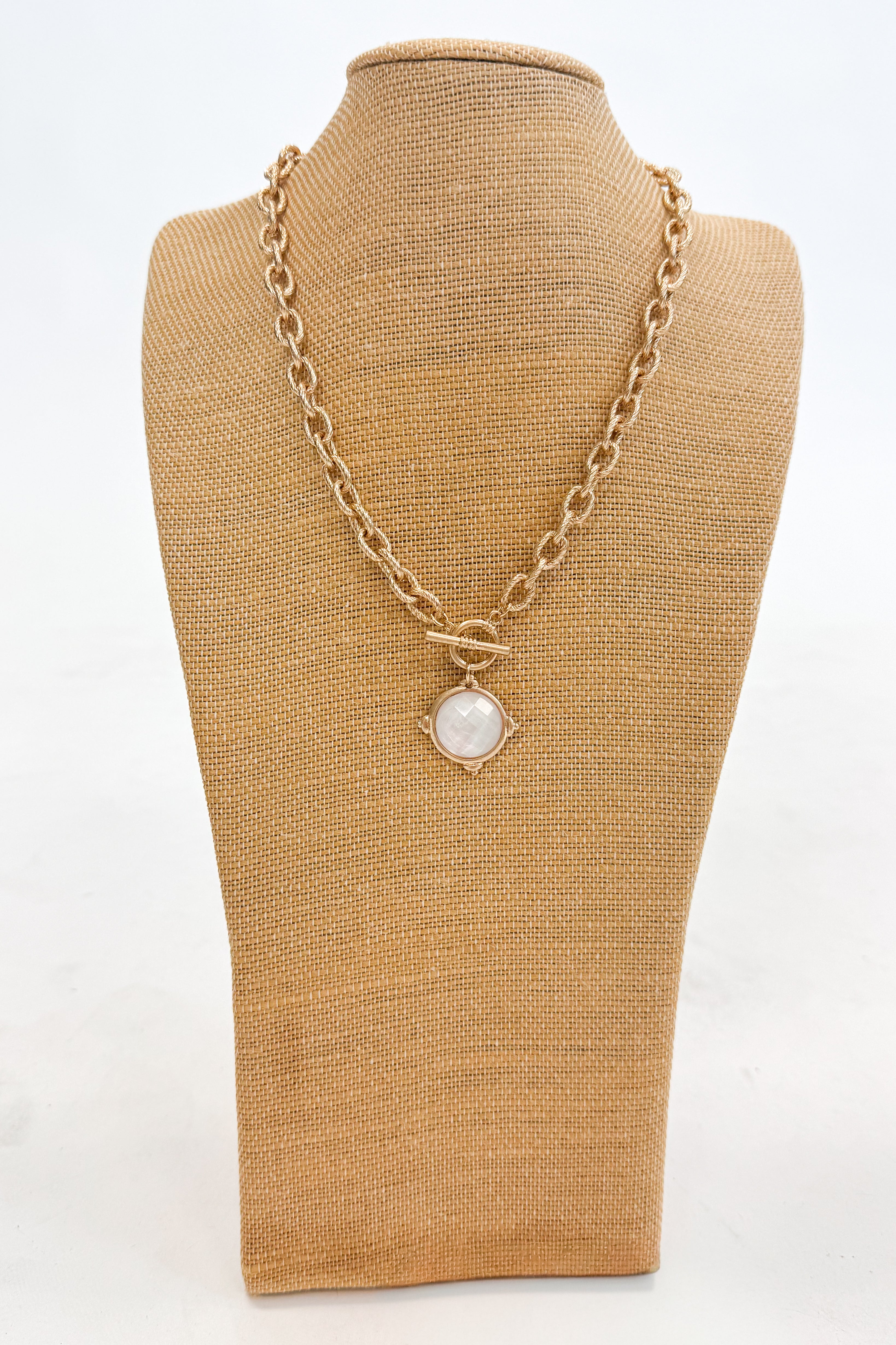 Gold chain necklace with a pendant on a brown mannequin bust against a white background