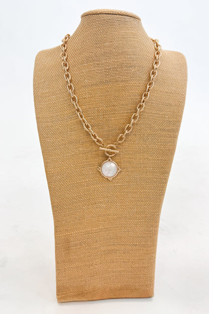 Gold chain necklace with a pendant on a brown mannequin bust against a white background