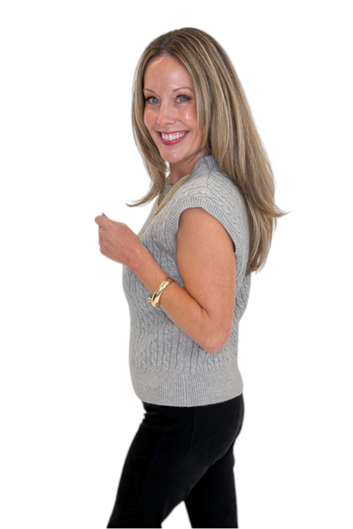 Side view of woman wearing Swagger Boutique’s Grey Cable Knit Denim Collared Sleeveless Sweater with jeans against white studio background.