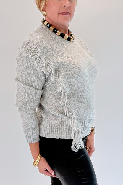 Side detail view of woman wearing Swagger Boutique’s Grey Fringe Sweater with jeans against white studio background.