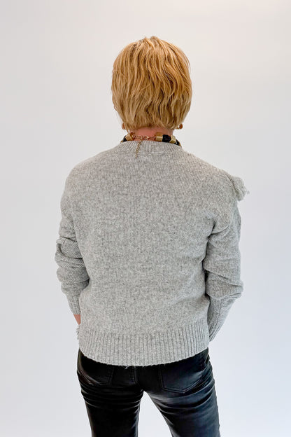 Back view of woman wearing Swagger Boutique’s Grey Fringe Sweater with jeans against white studio background.