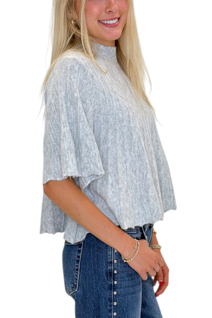 Side detail view of woman wearing Swagger Boutique’s Grey Ribbed Short Sleeve Sweater with jeans against white studio background.