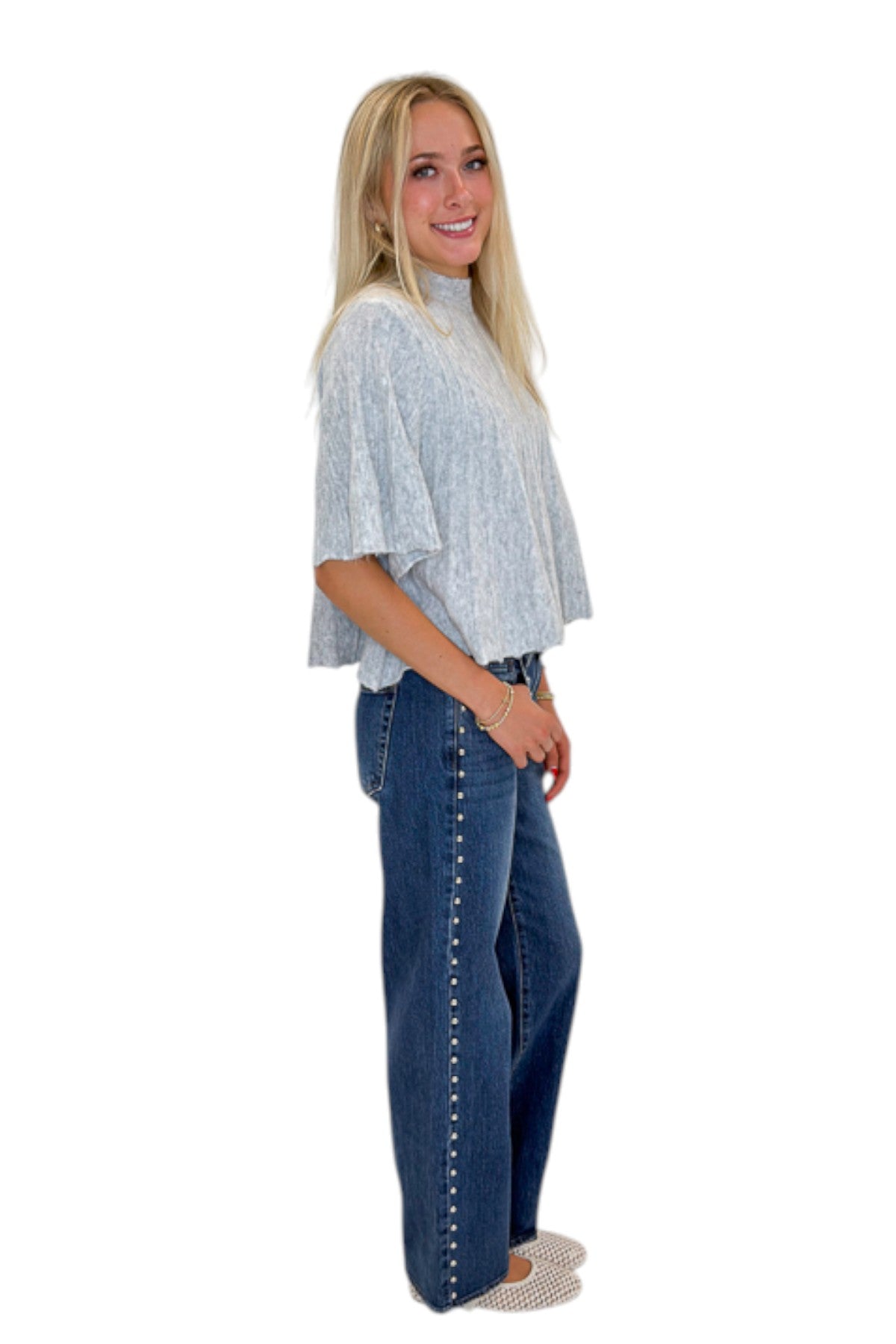 Side view of woman wearing Swagger Boutique’s Grey Ribbed Short Sleeve Sweater with jeans against white studio background.