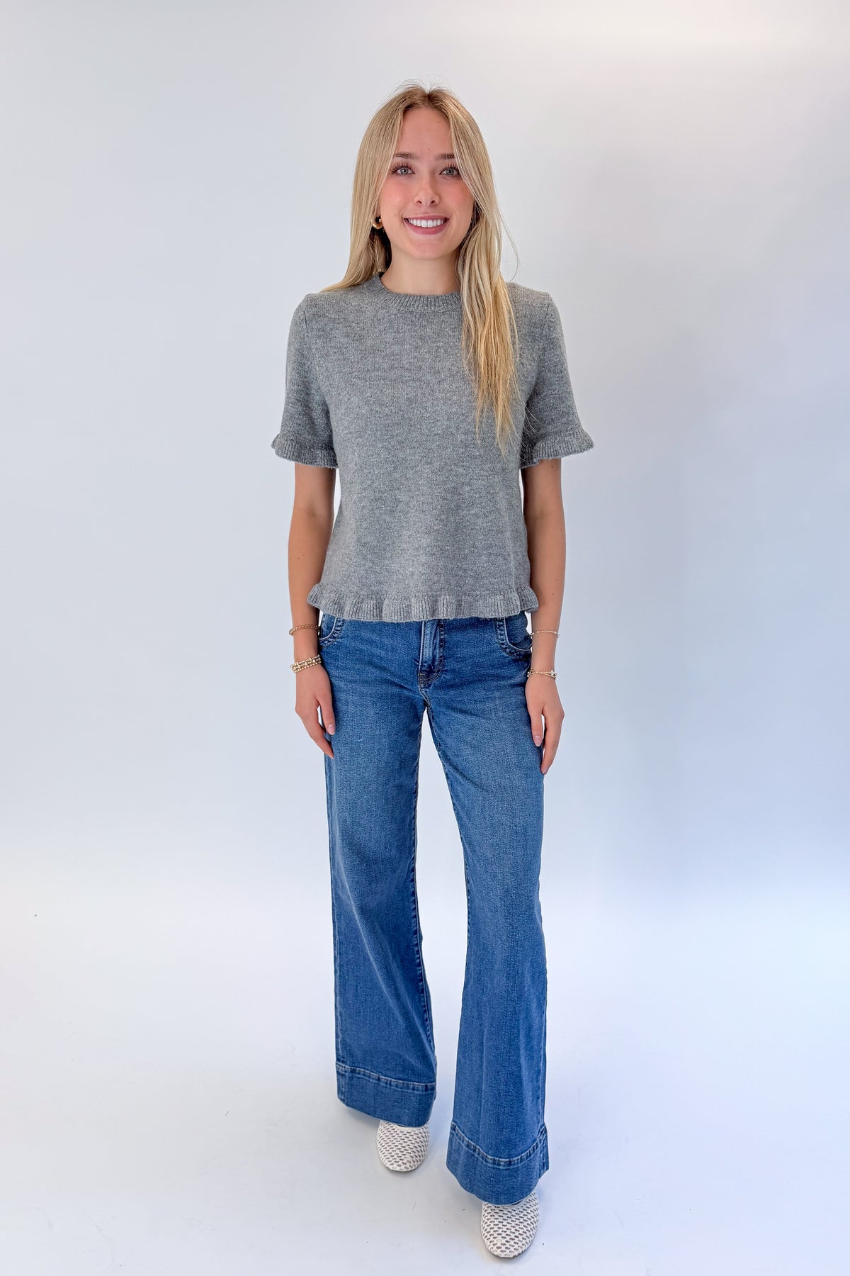 Front view of woman wearing Swagger Boutique’s Grey Ruffle Hem Sweater with jeans against white studio background.