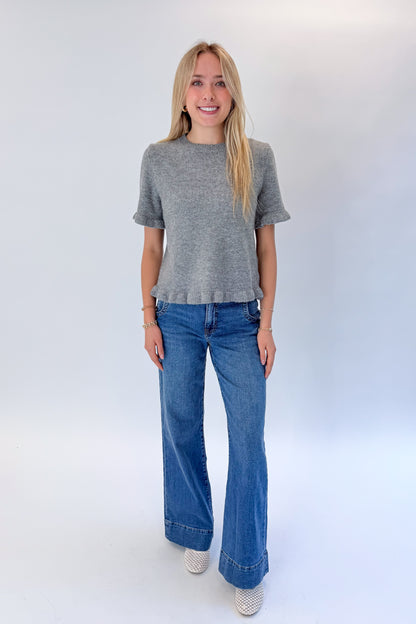 Front view of woman wearing Swagger Boutique’s Grey Ruffle Hem Sweater with jeans against white studio background.